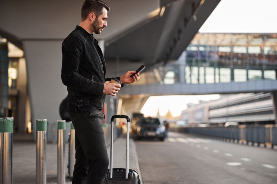Traveller with smartphone and coffee – Park & Fly for business trips in Vienna